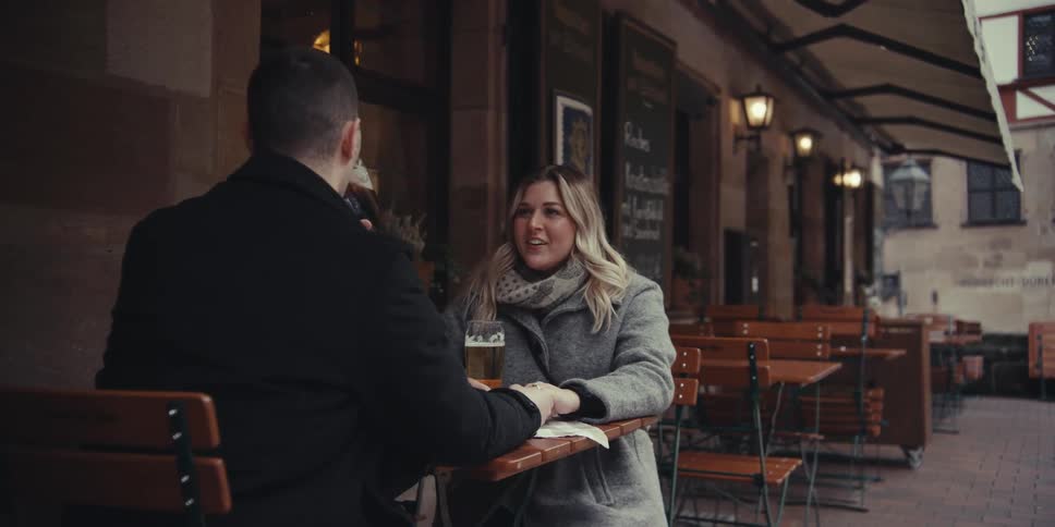 Couple talks at an outdoor caf table with a glass of beer on the table