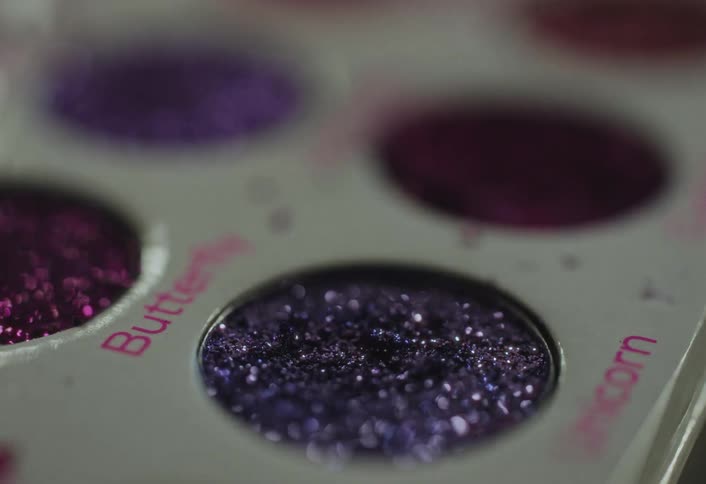 A makeup brush gently dips into a pan of shimmering purple eyeshadow highlighting the texture and sparkle of the pigment