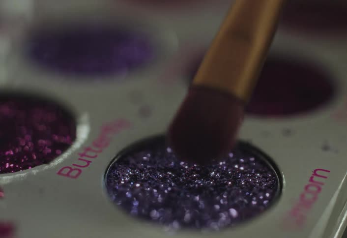 Brush touching a glitter eyeshadow pan in a makeup palette closeup