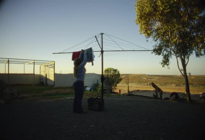 Person hangs clothes on a rotary clothesline in a rural outdoor area