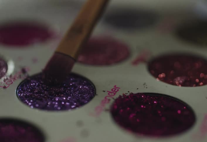 Brush touches purple glitter eyeshadow in a makeup palette