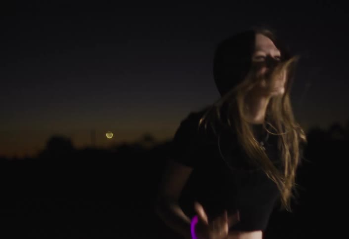 A woman dances joyfully under colorful lights at an outdoor night concert
