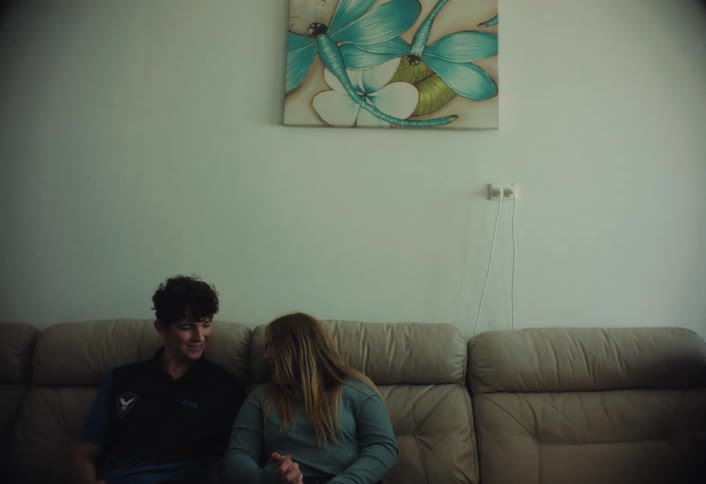 Siblings share a quiet conversation while sitting on a couch in a living room