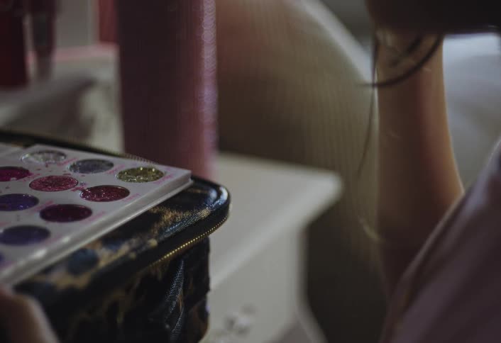 A young girl dips a mermaidthemed brush into a colorful glitter palette and carefully applies the shimmer to her face while sitting at a vanity