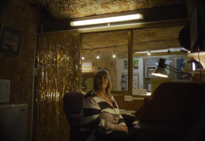 A woman sits calmly at a desk in a dimly lit space in an office