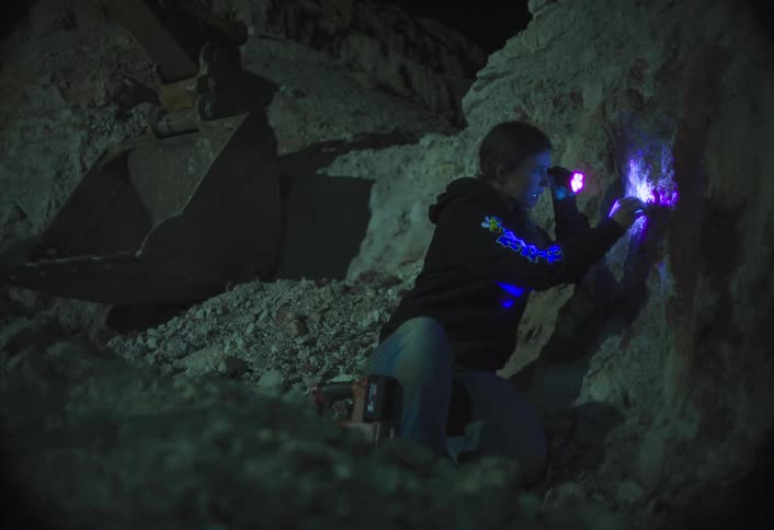 Teenager uses a special light to discover special materials near a digger at night