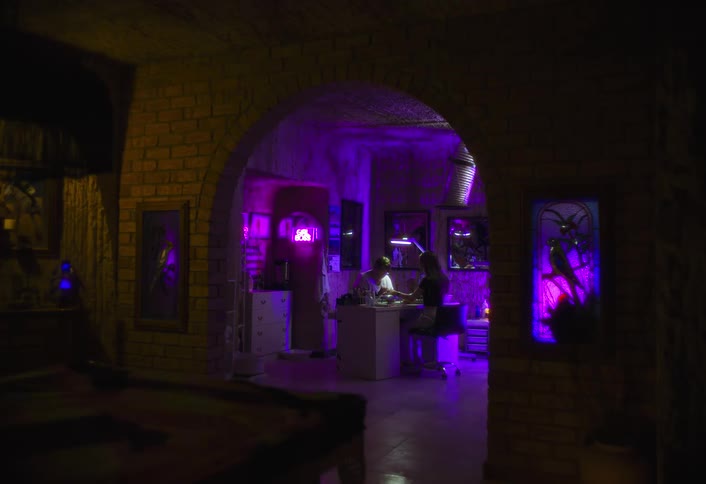 Indoor space with purple lighting shows people working at a counter beneath brick arches