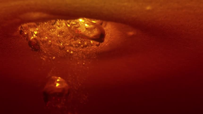 Glowing golden liquid forms abstract triangular textures as bubbles rise to the surface