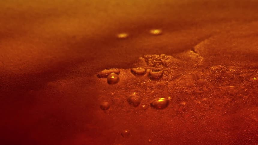 Golden liquid swirls into abstract textures as tiny bubbles rise on the surface