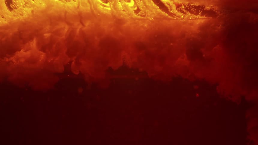 This video features a dark red liquid where a thick orangetinted cloud of substance billows and swirls from the top the motion creates a dramatic atmospheric effect similar to ink or sediment dispersing underwater