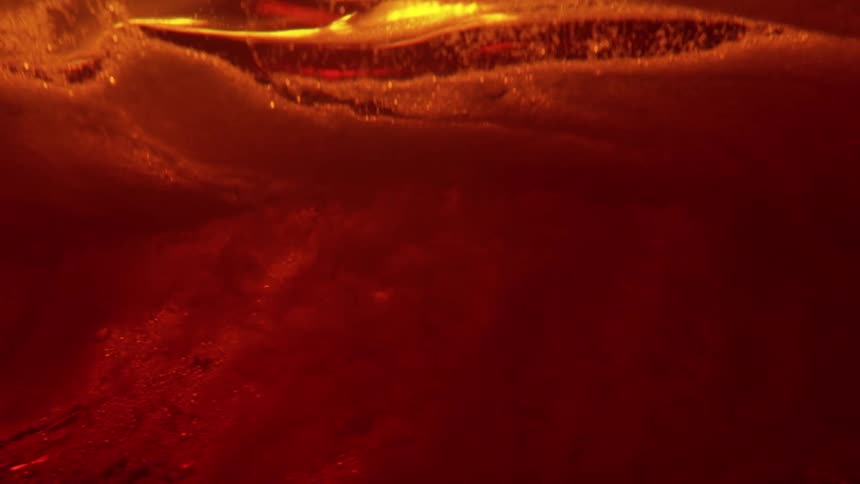 Closeup of amber liquid with a foamy layer and suspended particles