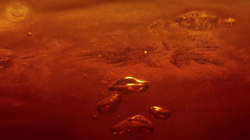 An ambercolored liquid swirls and churns creating a dense field of tiny shimmering particles and larger floating bubblesthe surface of the fluid ripples and undulates reflecting warm golden light as organic shapes merge and dissipate