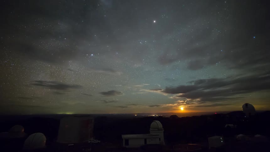 A starlit night sky with clouds drifting slowly as the darkness fades and dawn begins to form