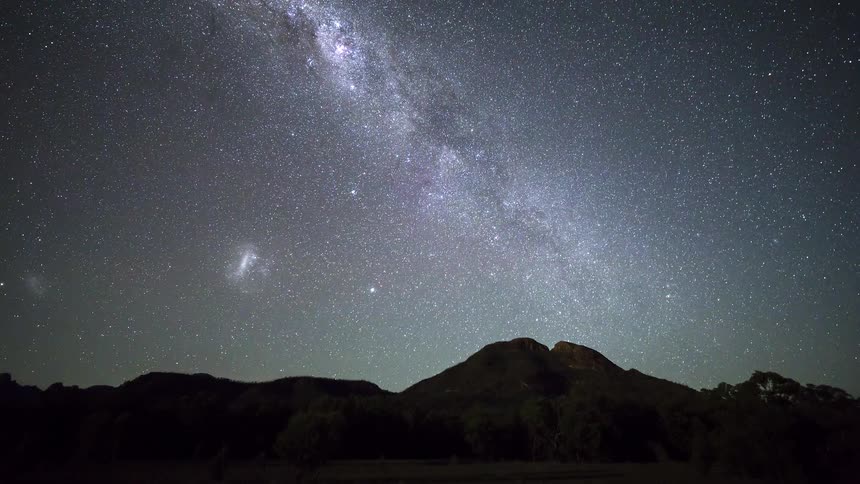There are two distinct lines visible within the compositionthe silhouette of a jagged mountain range creates a dark uneven horizontal line across the lower portion of the framea bright linear streak of light likely a meteor or satellite briefly