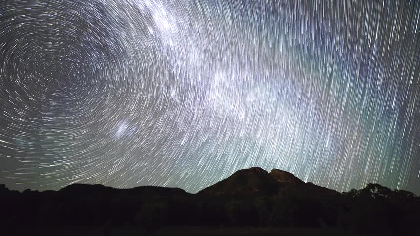 Long exposure stars form circular trails over a mountain landscape at night