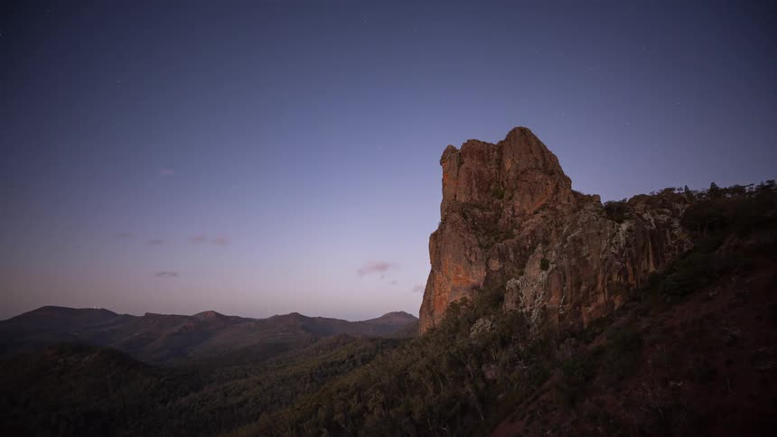 Day transitions to night in this spectacular timelapse as golden sunlight fades from a rugged rock monolith to reveal the mesmerizing rotation of the milky way galaxy across the starry sky