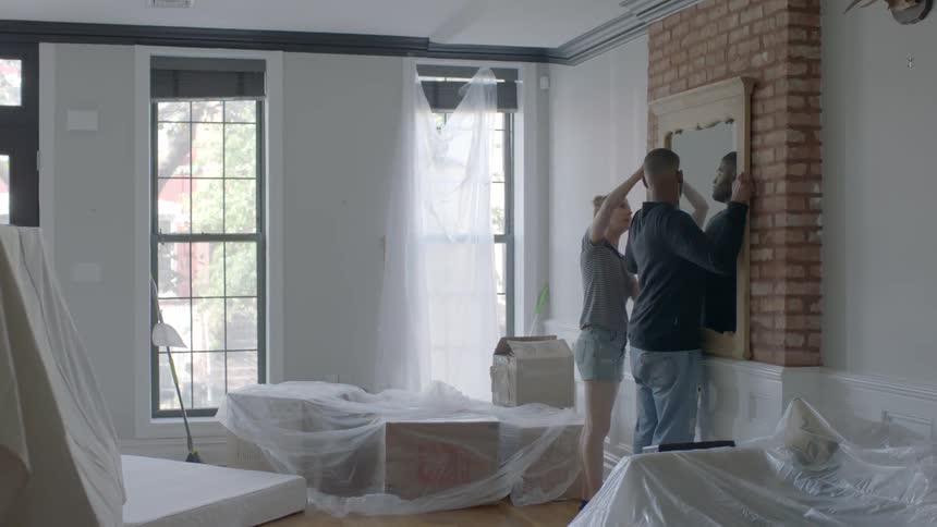 A man and woman hang a mirror on the wall