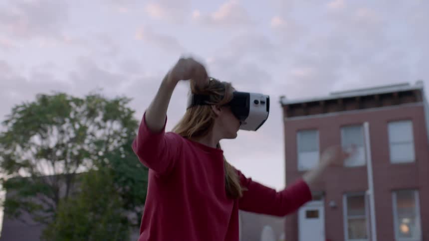 A woman uses a virtual reality headset outside at sunset