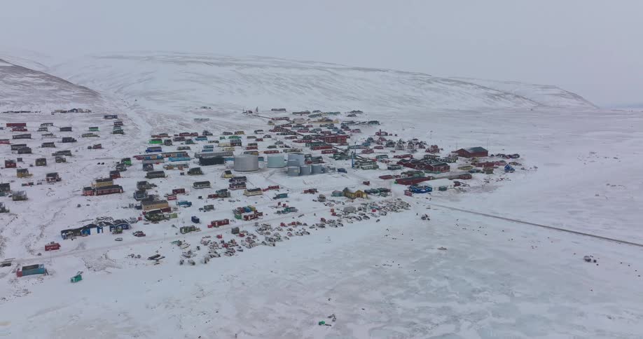 Polar settlement covered in snow with colorful buildings spread across a plain and hillside