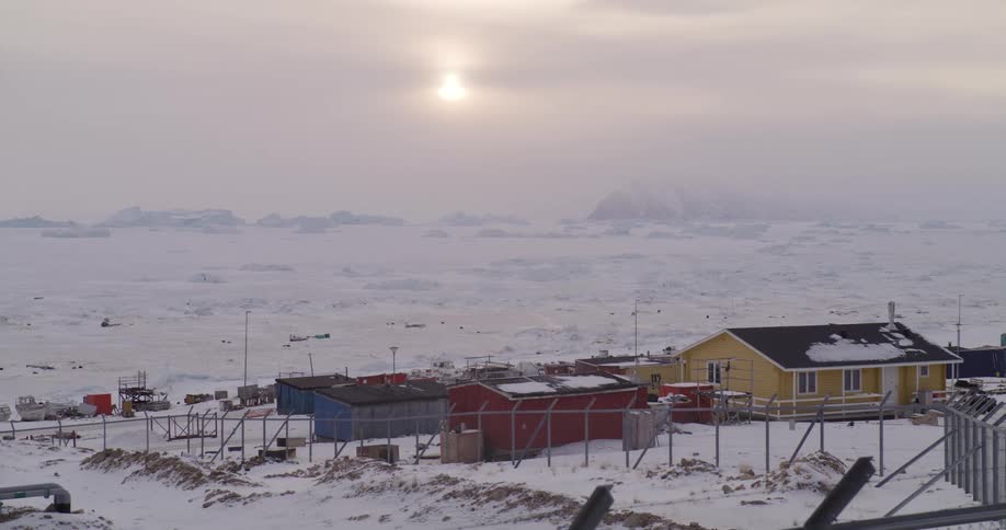 Coastal infrastructure in a polar region covered with snow featuring colorful buildings under a cloudy sky