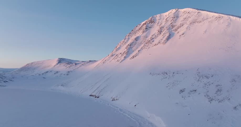 Sunlight shines on a snow covered mountain under a clear blue sky