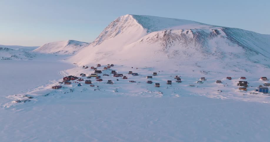 Remote settlement in a snowcovered region at the base of mountains under a clear sky