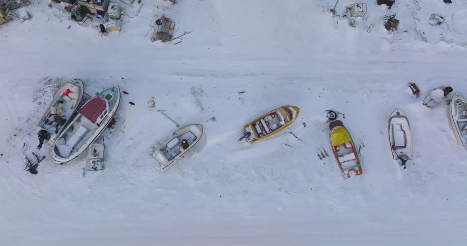 A series of boats sit frozen in place on a lake locked into the ice on a winter day