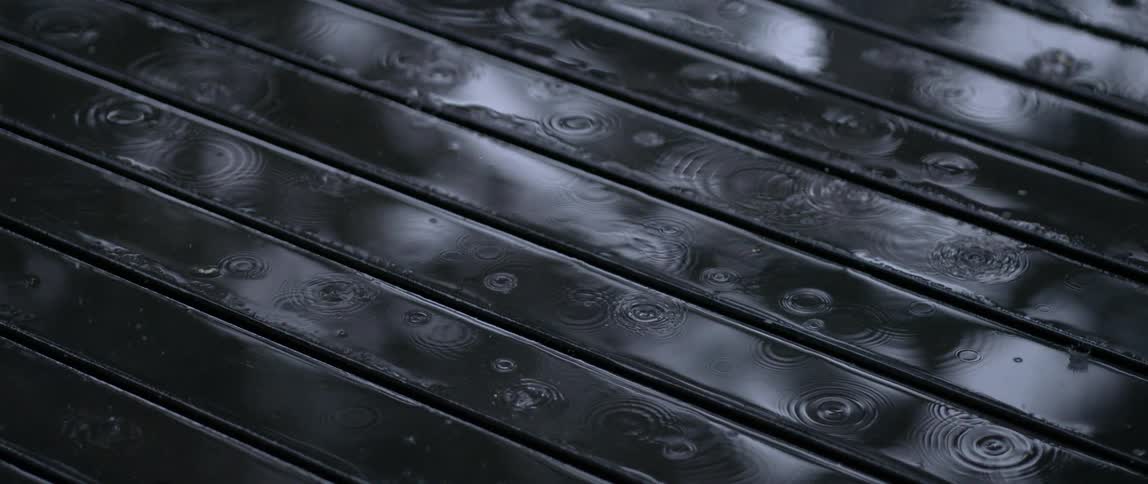 Rain falls onto the water puddling on a wooden deck creating ripples during the daytime
