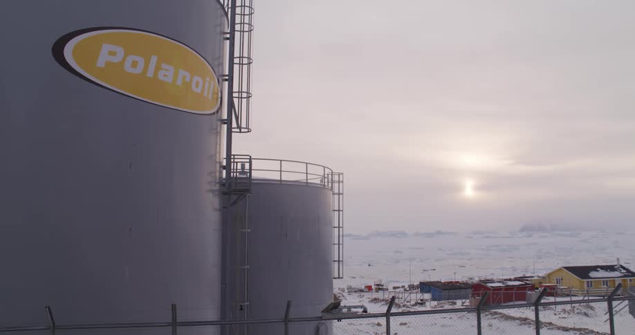 Houses stand on a snowy plain near large polaroil tanks on a winter day