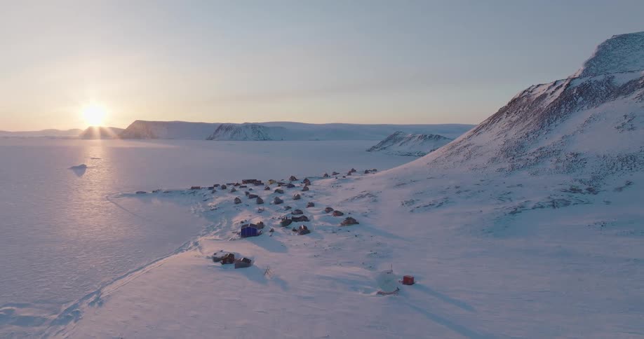 Sun shines across the water and onto a coastal town located near the base of a snowy mountain on a winter day