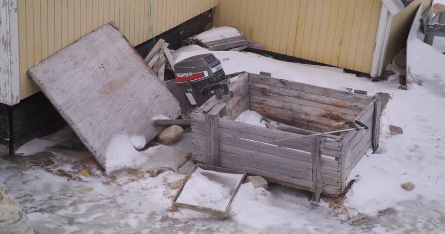 Damaged wooden structure with an outboard motor and accumulated snow beside a building