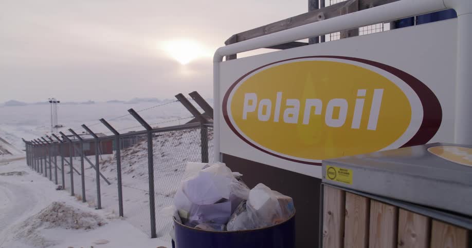 Polaroil sign on a fence with buildings in the distance on the arctic coast