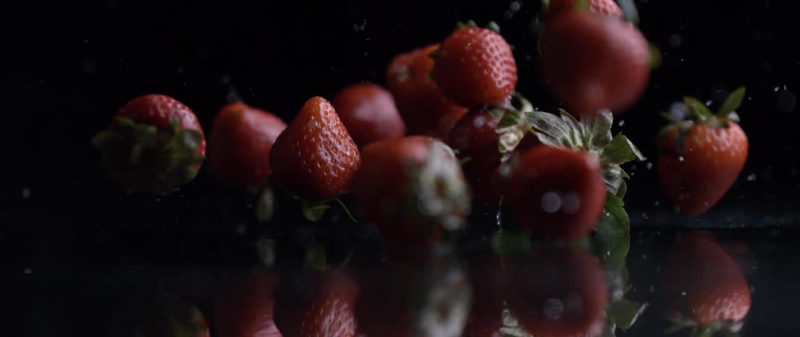 Strawberries falling onto a reflective surface with water splashes against a dark background
