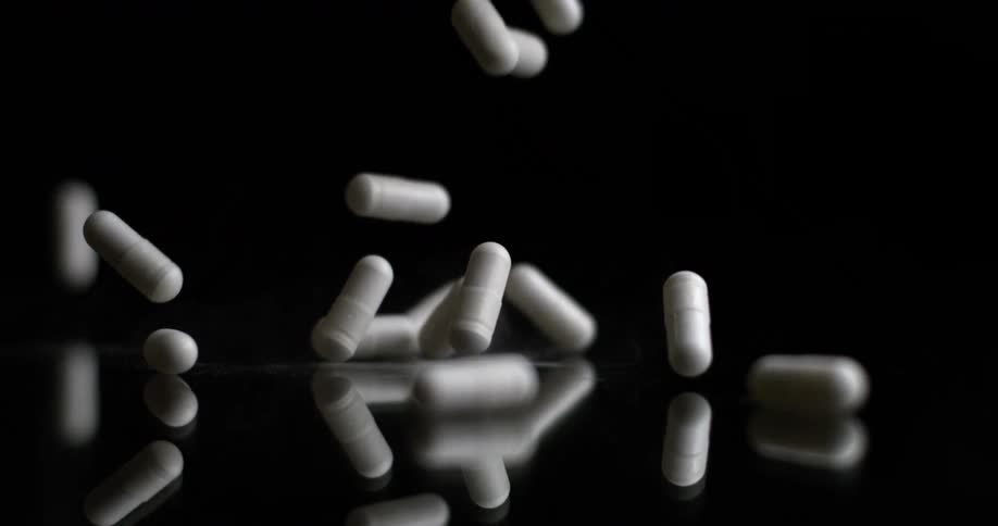White capsules falling onto a reflective surface against a dark background
