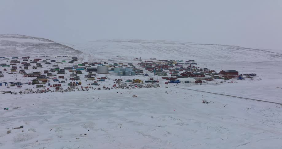 Remote settlement covered in snow across a wide plain with buildings spread along the hillside
