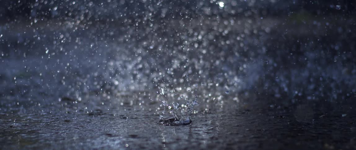 Light shines on raindrops falling and splashing into the water