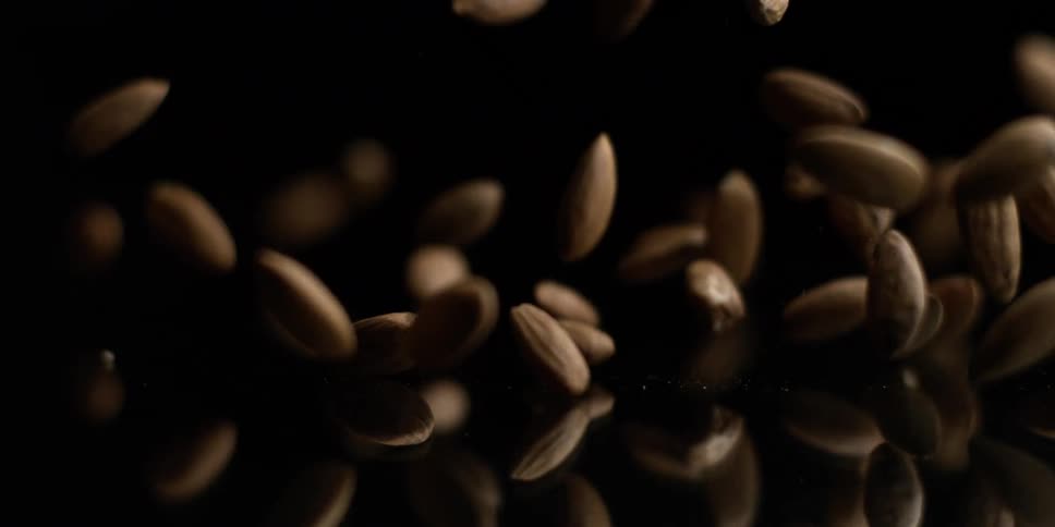 Almonds falling onto a reflective surface against a dark background