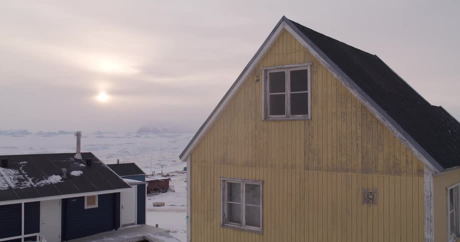 Houses overlook the frozen arctic coast as the sun shines though clouds in the distance