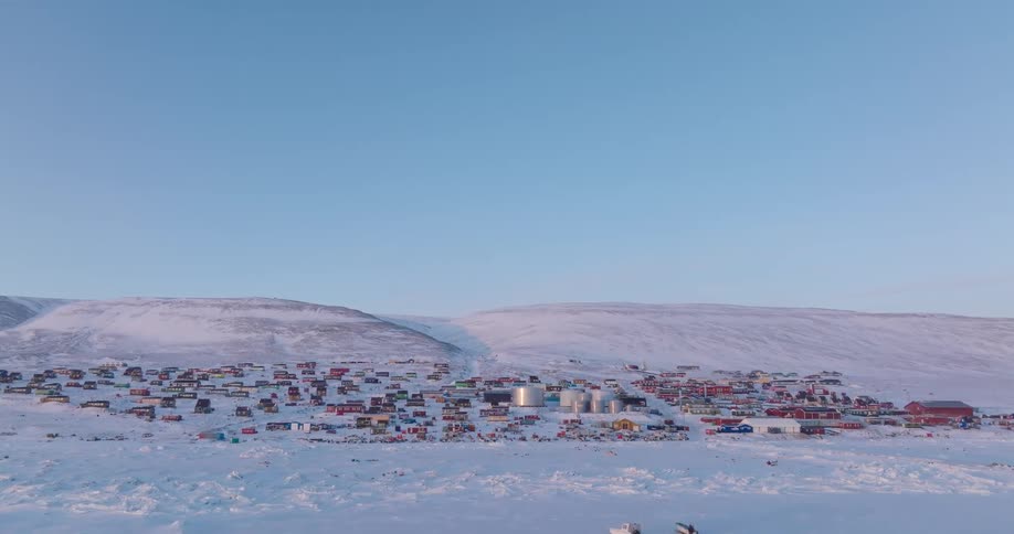Snowcovered polar settlement with colorful buildings spread between hills under a blue sky