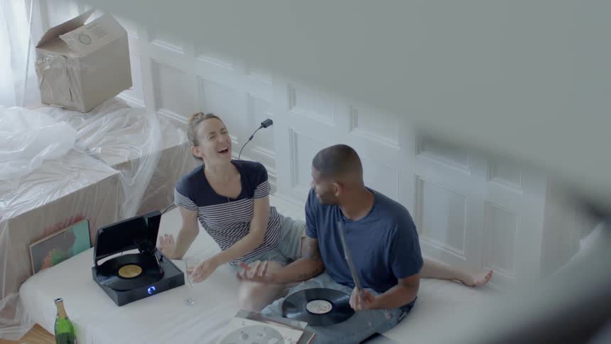 A man and woman sit on a mattress playing record albums and laughing