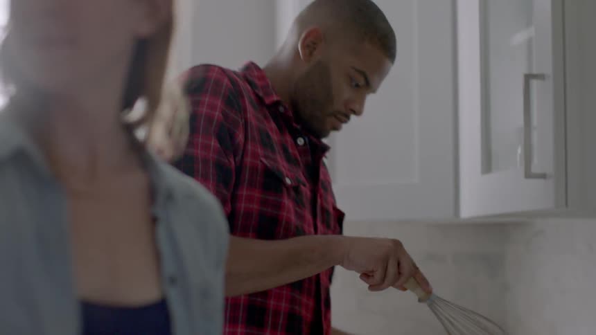 Man mixing something in a bowl in the kitchen with a woman nearby