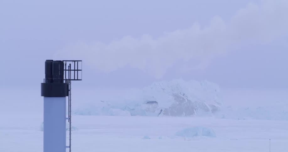 Smoke from a tower chimney overlooking the frozen arctic moves across the sky