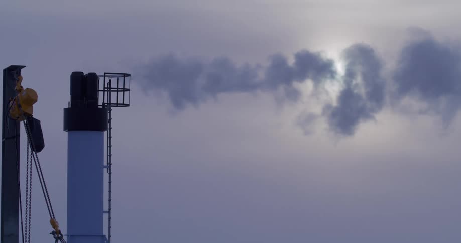 Dark smoke billows from the tall smokestack of a ship into a hazy sky with the sun visible through the clouds
