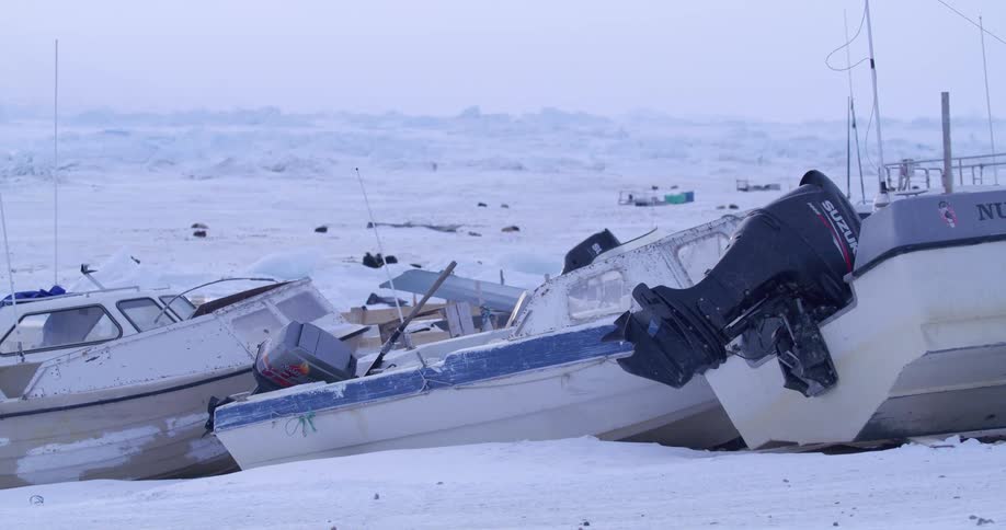 Several boats are idle on land in a snow covered landscape
