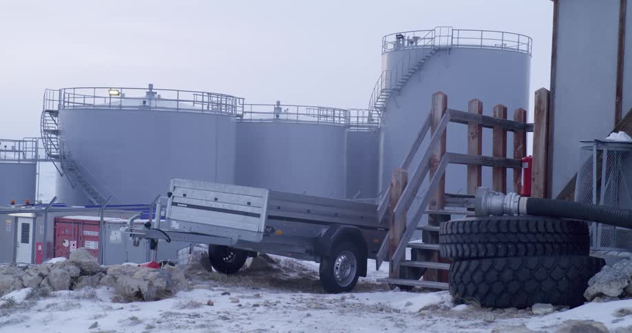 Trailer parked at an industrial facility with metal storage tanks in a snowcovered area