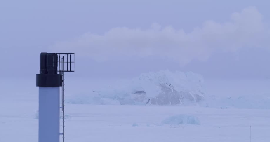 Smoke flows from a narrow chimney towering over a snowy landscape on a winter day