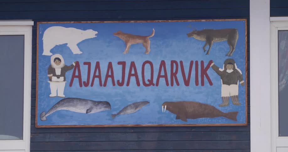 A stationary shot shows a blue building exterior featuring a mural surrounded by painted arctic animals and two figures in traditional parkas