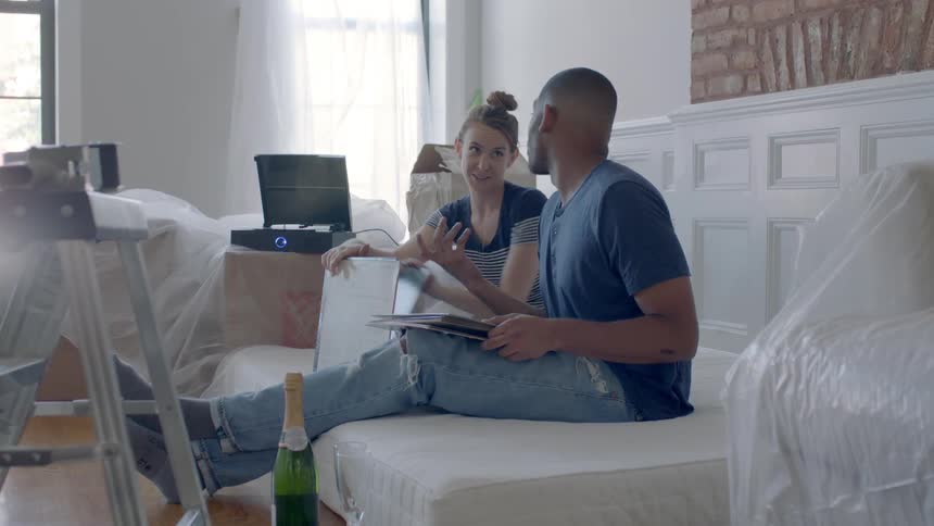 A man and woman look at records while sitting on a mattress on the floor