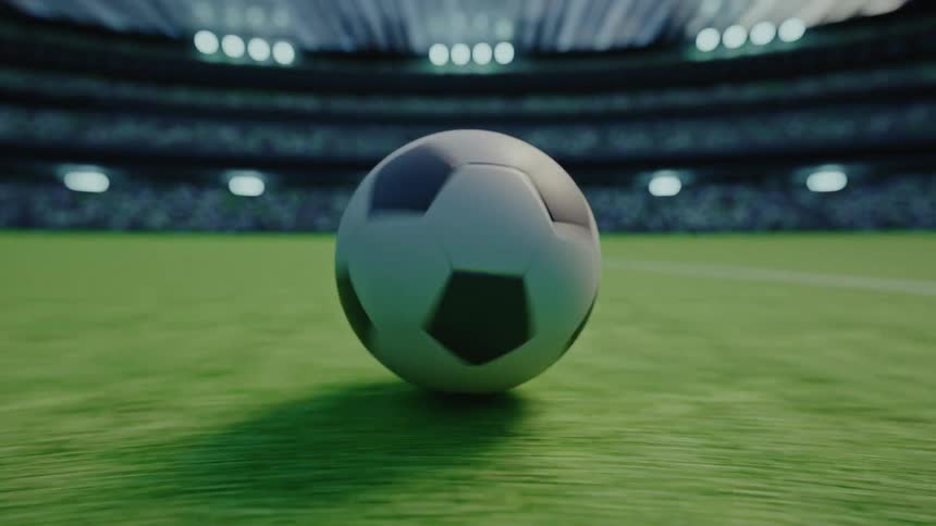 Soccer ball rolling on the grass with a lit stadium in the background