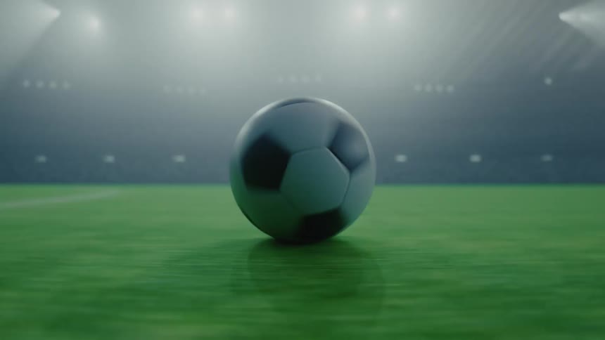 Soccer ball rolling in the center of a pitch under stadium lighting